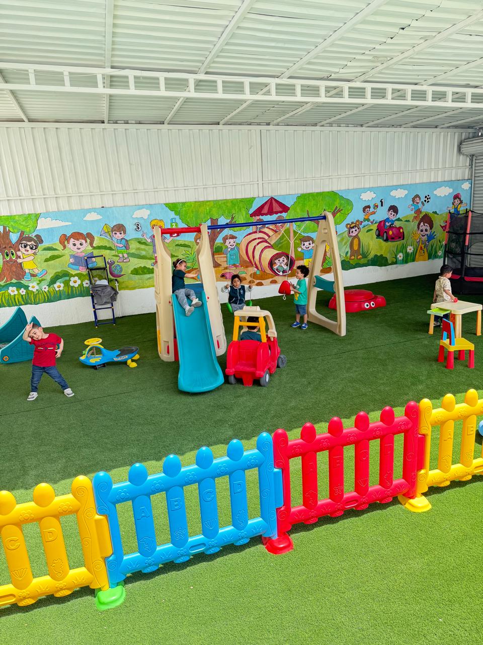 Indoor playground with colorful slide, swings, soft fence, and educational mural at Early Scholars Nursery